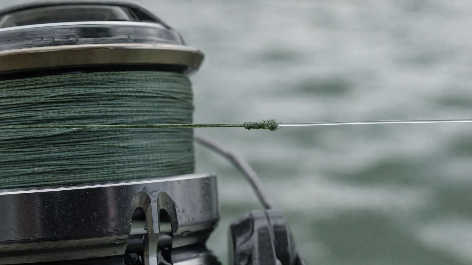 Close-up of a slim braid-to-fluorocarbon leader knot lying across the lip of a loaded spinning reel spool
